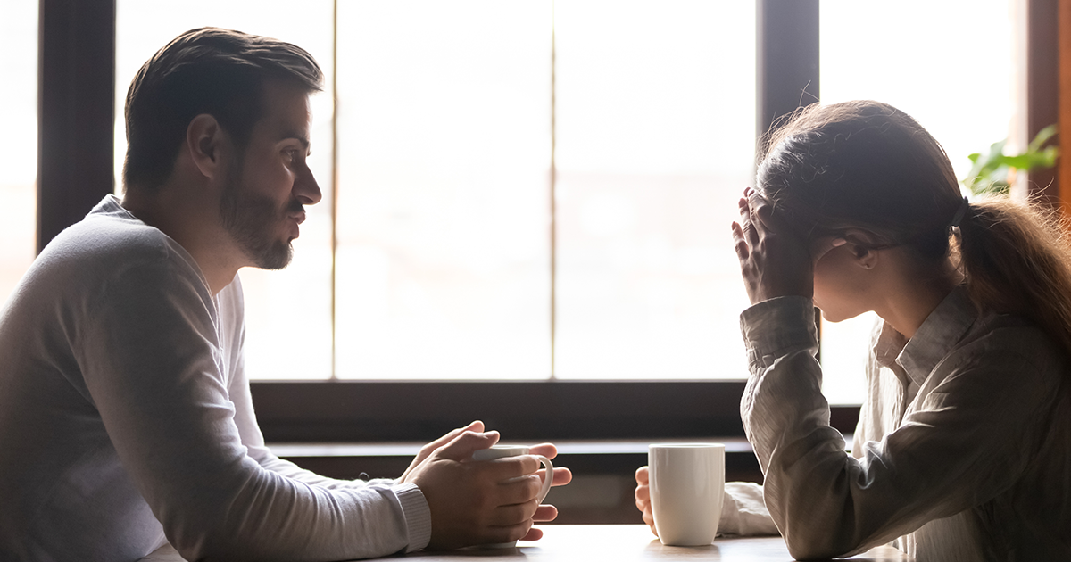 A man and a woman sat at a table talking whilst having a hot drink