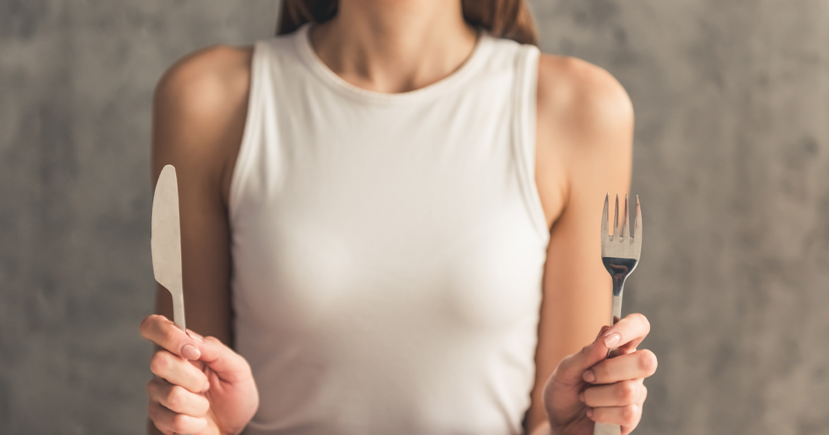 Lady sat down at a dining table holding a knife and fork