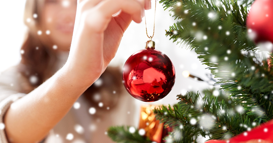 A lady decorating a Christmas tree with a red bauble