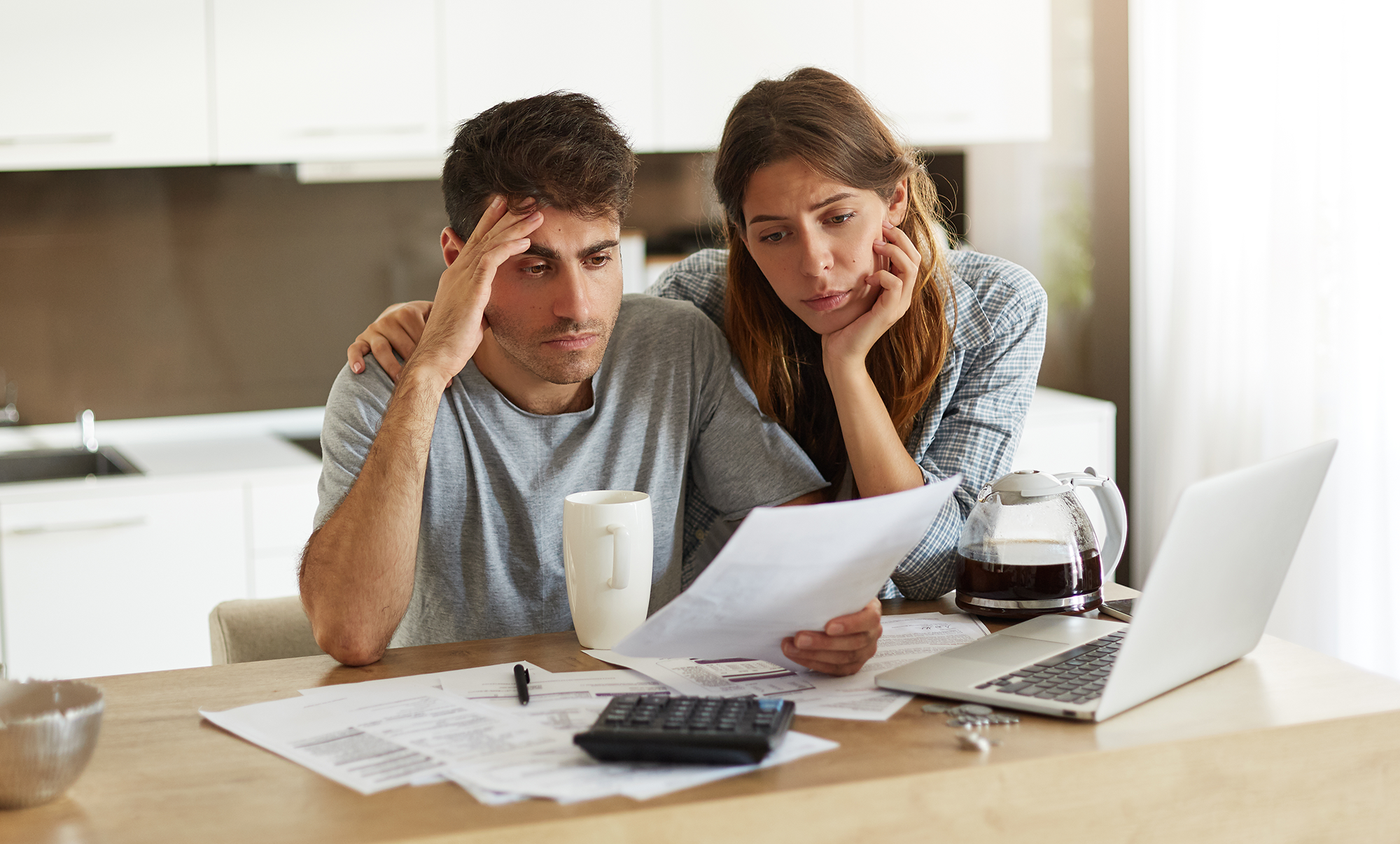 A man and woman looking at bills whilst sat at a kitchen counter
