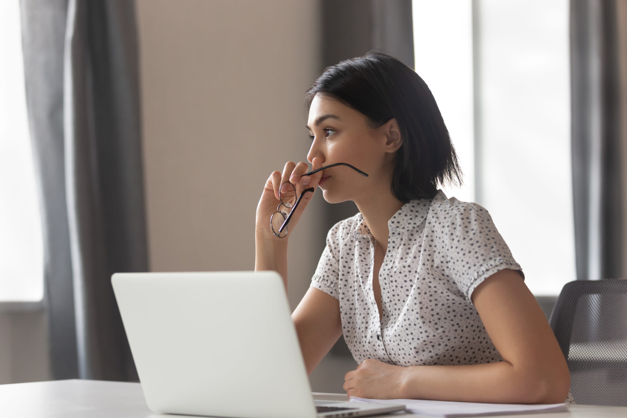 A lady sat in front of a laptop whilst thinking